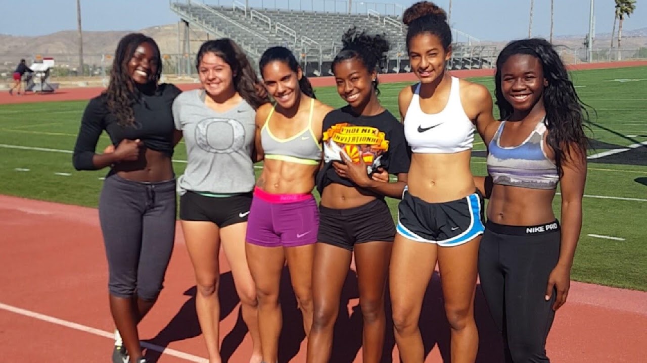 Ashley and a group of athletes standing together and smiling on a running track